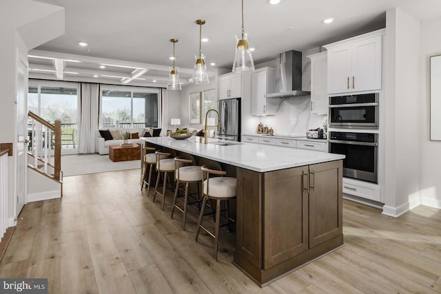 kitchen with a spacious island, coffered ceiling, a sink, wall chimney range hood, and appliances with stainless steel finishes