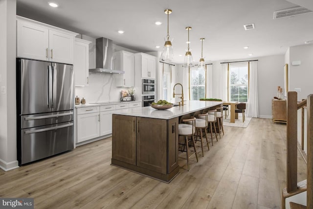 kitchen featuring a kitchen island with sink, visible vents, wall chimney range hood, and stainless steel refrigerator