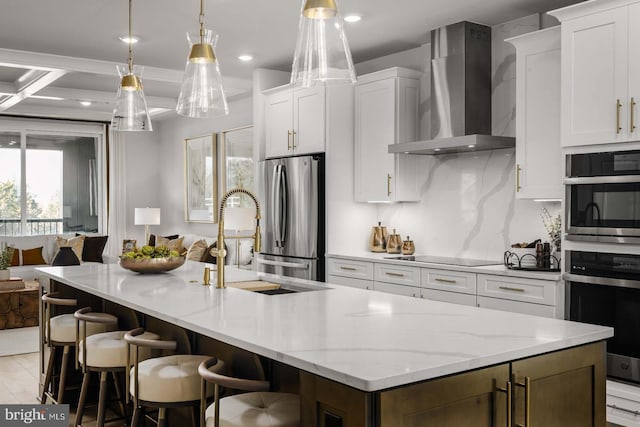 kitchen featuring a kitchen island with sink, wall chimney range hood, appliances with stainless steel finishes, and white cabinets