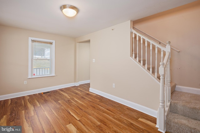 spare room with visible vents, stairway, baseboards, and wood finished floors