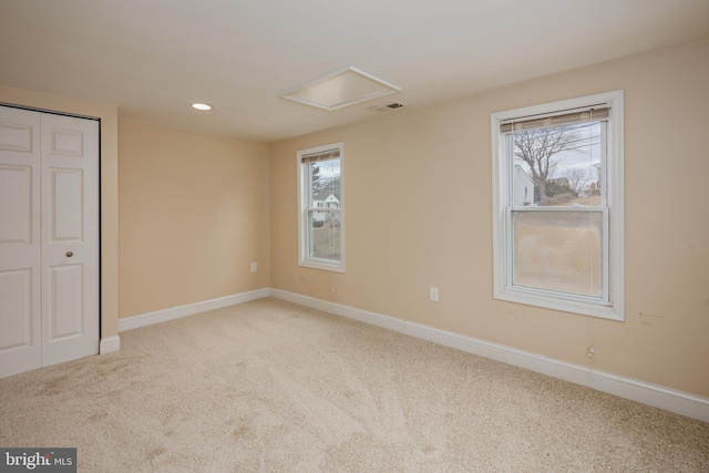 unfurnished bedroom featuring multiple windows, carpet flooring, visible vents, and attic access