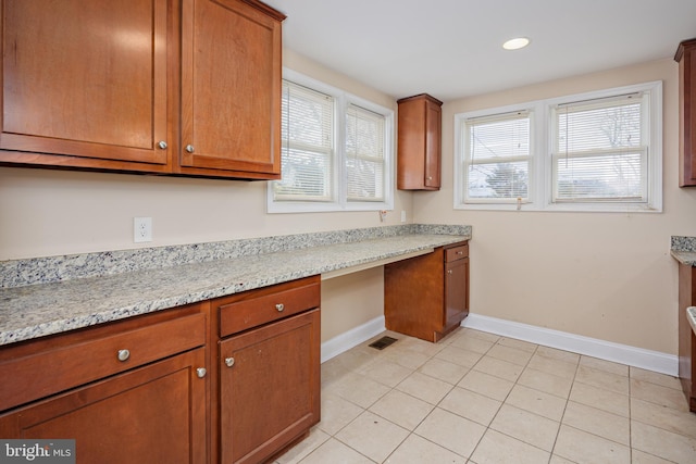 kitchen with brown cabinetry, built in study area, baseboards, and light tile patterned floors