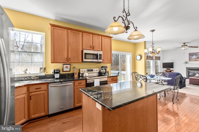 kitchen with light wood-type flooring, stainless steel appliances, open floor plan, and decorative light fixtures