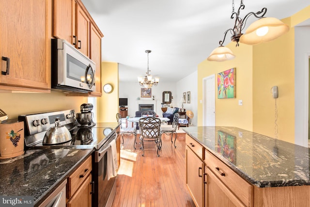 kitchen with light wood finished floors, stainless steel appliances, brown cabinetry, a fireplace, and hanging light fixtures