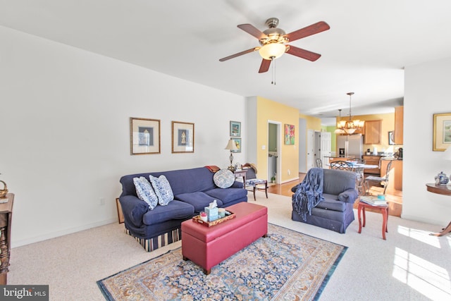 living room featuring ceiling fan with notable chandelier, baseboards, and carpet