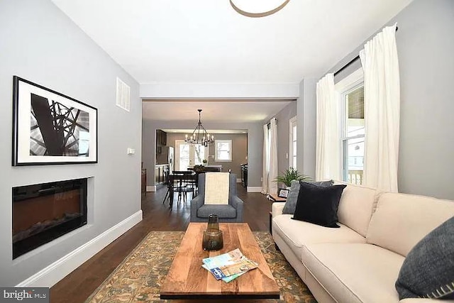 living room featuring dark wood-style floors, a glass covered fireplace, visible vents, and baseboards