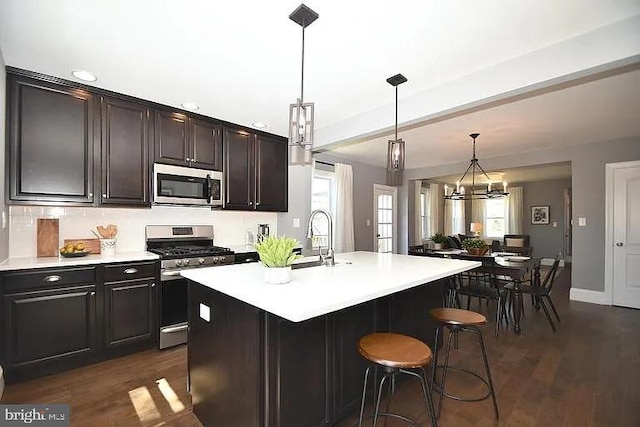 kitchen with a breakfast bar area, a sink, light countertops, appliances with stainless steel finishes, and dark wood finished floors