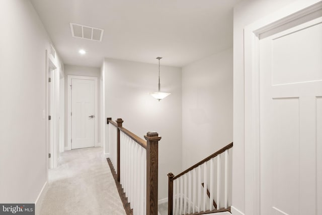 hallway with carpet floors, baseboards, visible vents, and an upstairs landing