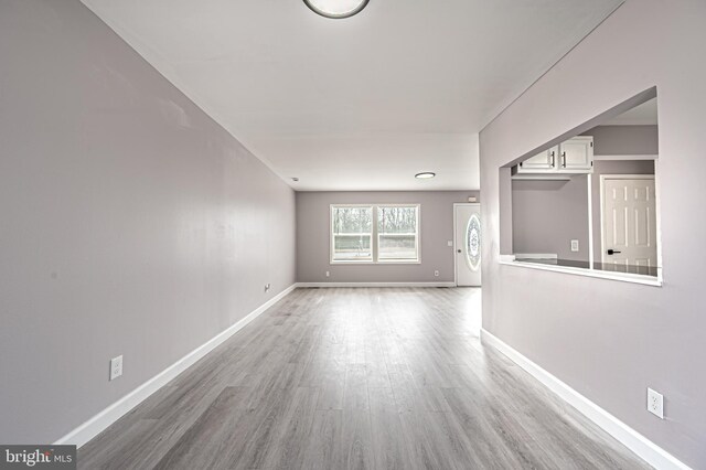 unfurnished living room with light wood-type flooring and baseboards