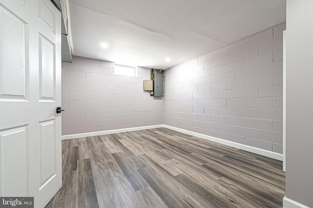 basement with concrete block wall, electric panel, baseboards, dark wood-type flooring, and recessed lighting