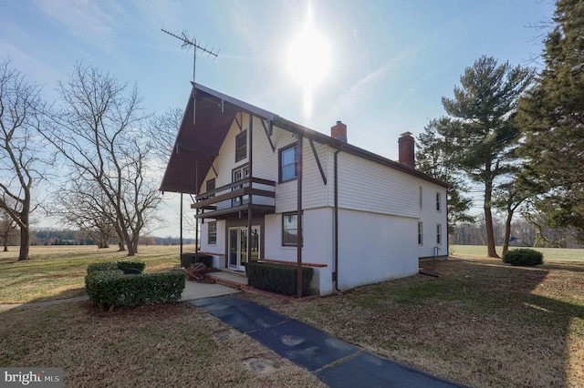 view of home's exterior featuring a yard, a chimney, and a balcony