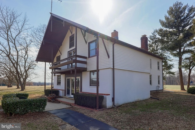 view of front facade with a balcony, a chimney, and french doors