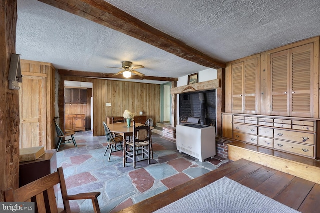 dining room with beam ceiling, heating unit, stone finish floor, wood walls, and a textured ceiling