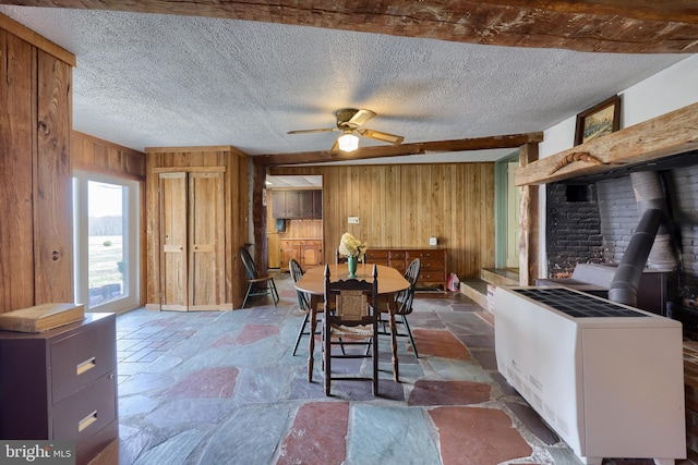 dining area featuring a wood stove, stone tile floors, wooden walls, and a textured ceiling