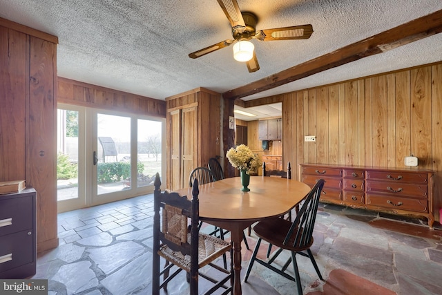 dining space featuring beamed ceiling, wooden walls, stone tile floors, and a textured ceiling