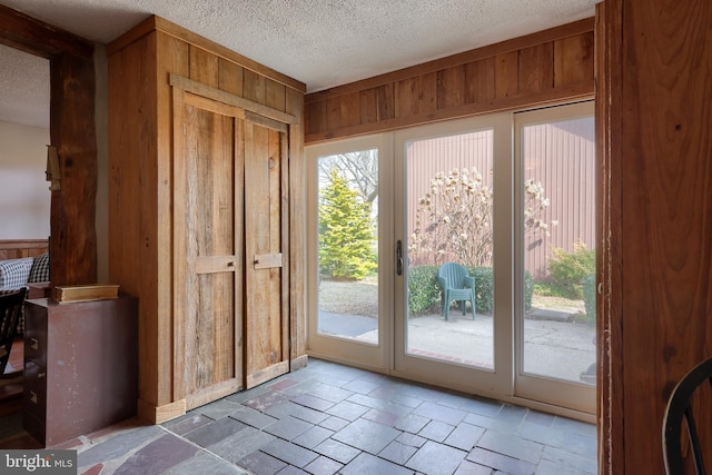 entryway with a textured ceiling, wood walls, and stone tile flooring