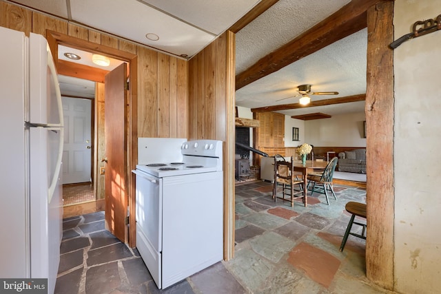 kitchen with stone tile flooring, a ceiling fan, wooden walls, a textured ceiling, and white appliances