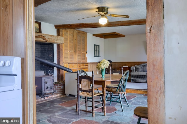 dining room with a textured ceiling, a wainscoted wall, stone tile flooring, beam ceiling, and a wood stove