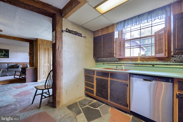 kitchen with stone tile floors, light countertops, a sink, a drop ceiling, and dishwasher