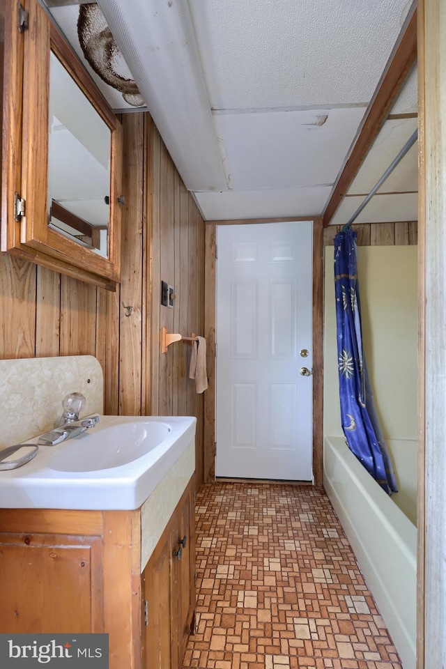 full bathroom with brick floor, wooden walls, shower / bath combination with curtain, and vanity