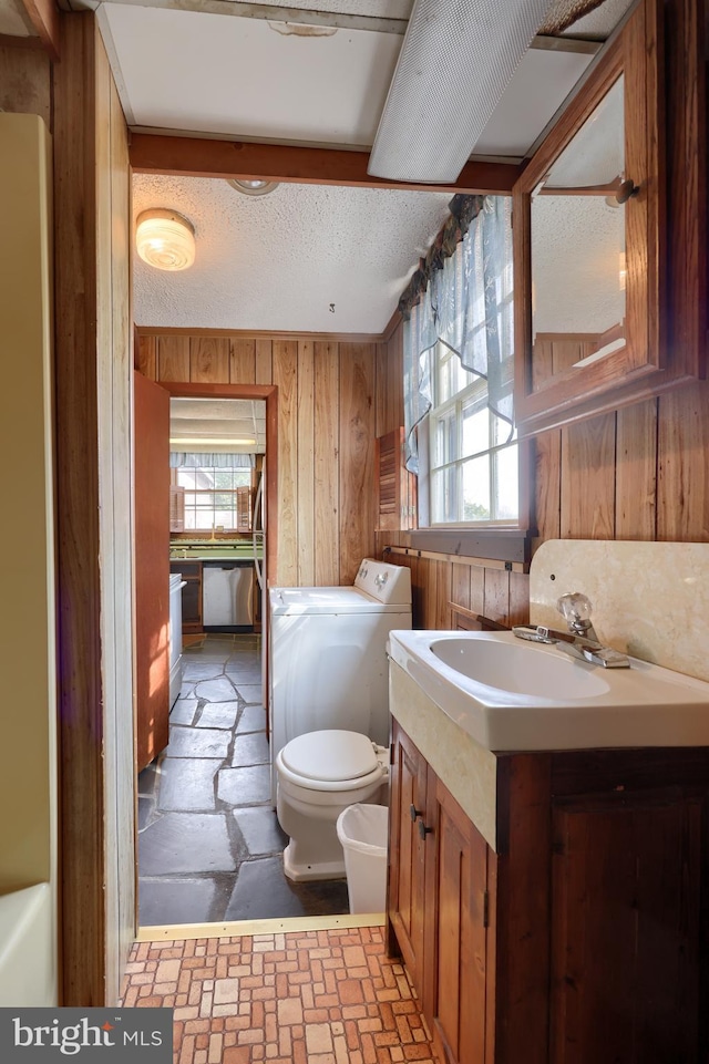 bathroom featuring toilet, wood walls, washing machine and dryer, and a wealth of natural light