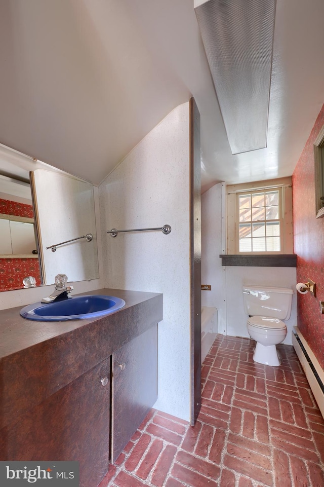 full bathroom with brick floor, toilet, a baseboard heating unit, vanity, and a bathtub