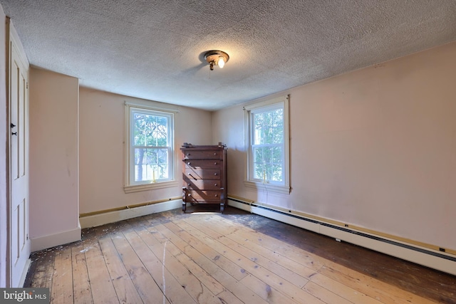 spare room featuring a textured ceiling, baseboard heating, hardwood / wood-style flooring, and baseboards