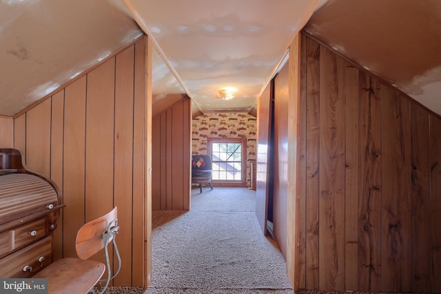 hallway with carpet floors, lofted ceiling, and wooden walls