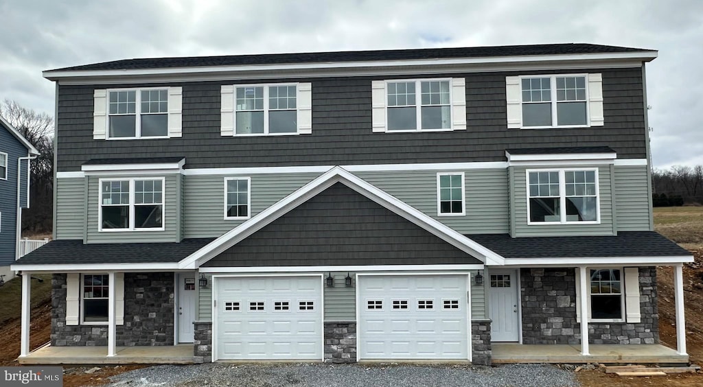 view of front of home with a porch, stone siding, driveway, and a garage