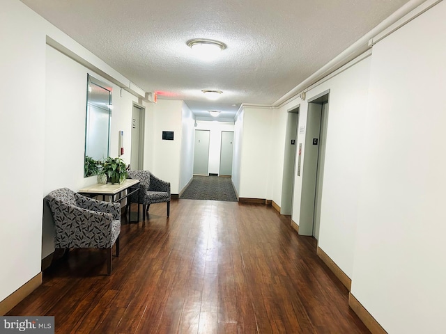 hall featuring a textured ceiling, dark wood-style flooring, elevator, and baseboards