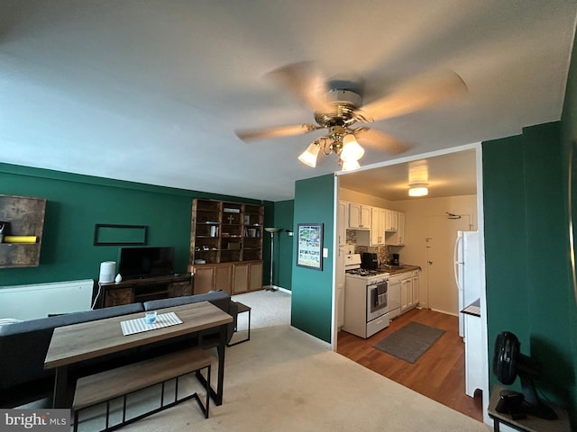 kitchen featuring white appliances, decorative backsplash, white cabinets, a ceiling fan, and wood finished floors