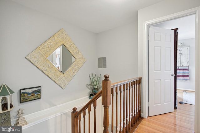 hall featuring wood finished floors, an upstairs landing, and visible vents