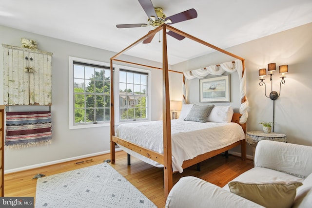 bedroom with a ceiling fan, wood finished floors, visible vents, and baseboards