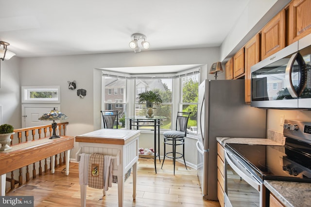 kitchen with light wood-type flooring, brown cabinetry, baseboards, and stainless steel appliances