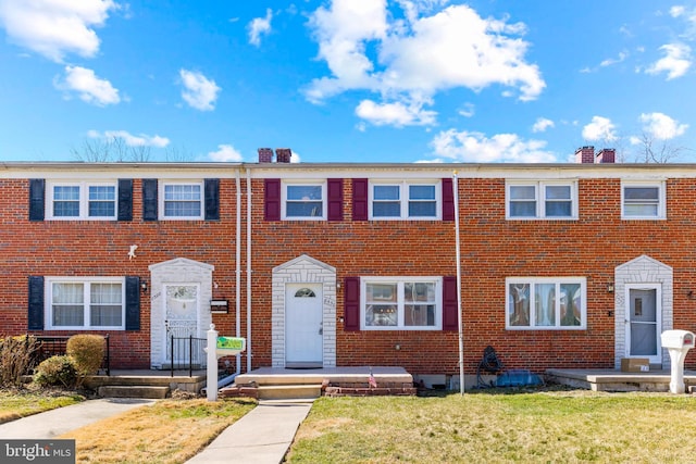 multi unit property with a front yard, brick siding, and a chimney