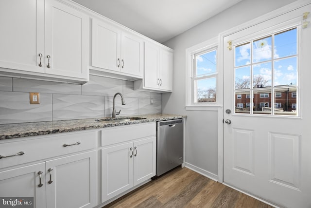 kitchen featuring stone countertops, wood finished floors, stainless steel dishwasher, white cabinetry, and a sink