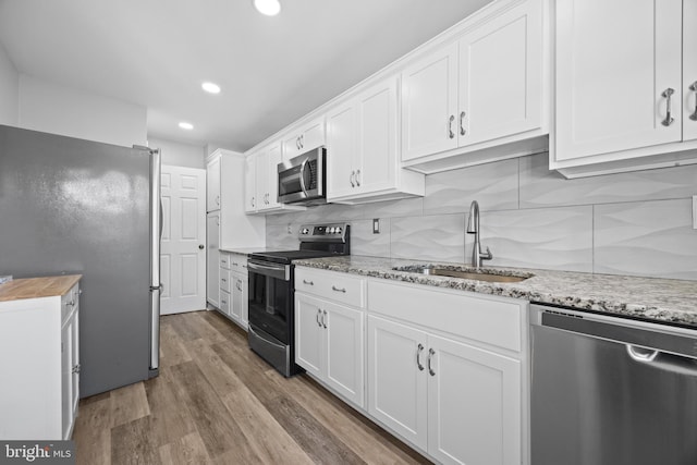 kitchen featuring tasteful backsplash, appliances with stainless steel finishes, wood finished floors, white cabinetry, and a sink