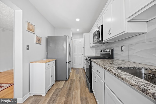 kitchen with white cabinets, light stone counters, stainless steel appliances, light wood-style floors, and backsplash