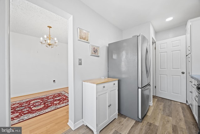 kitchen featuring white cabinets, light wood-style flooring, freestanding refrigerator, a chandelier, and recessed lighting