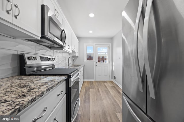 kitchen with light wood-style flooring, a sink, stainless steel appliances, white cabinetry, and backsplash