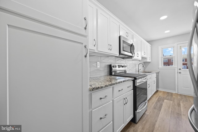 kitchen featuring light wood-style flooring, stainless steel appliances, a sink, white cabinets, and decorative backsplash