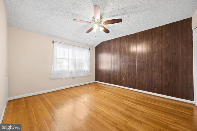 empty room featuring a textured ceiling, wooden walls, a ceiling fan, and wood finished floors