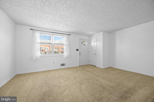 carpeted empty room featuring visible vents, a textured ceiling, and baseboards