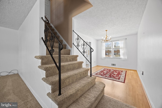 staircase featuring visible vents, a textured ceiling, wood finished floors, a chandelier, and baseboards