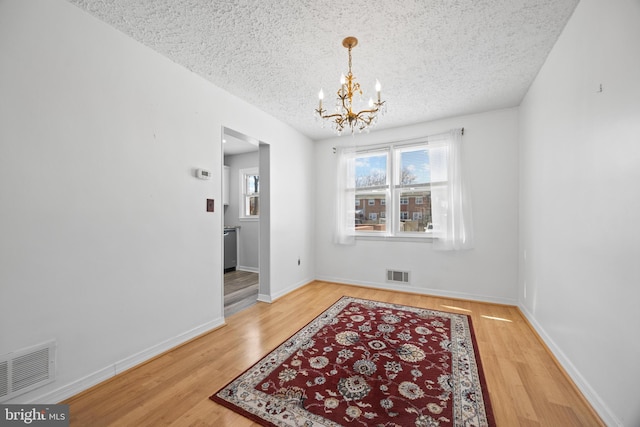 dining area with a textured ceiling, visible vents, a chandelier, and wood finished floors