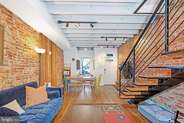 living area with brick wall, stairs, wood-type flooring, and track lighting
