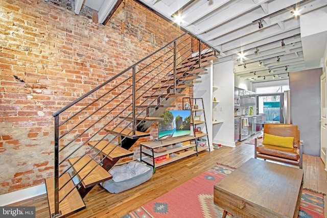interior space with track lighting, brick wall, hardwood / wood-style flooring, and stairs