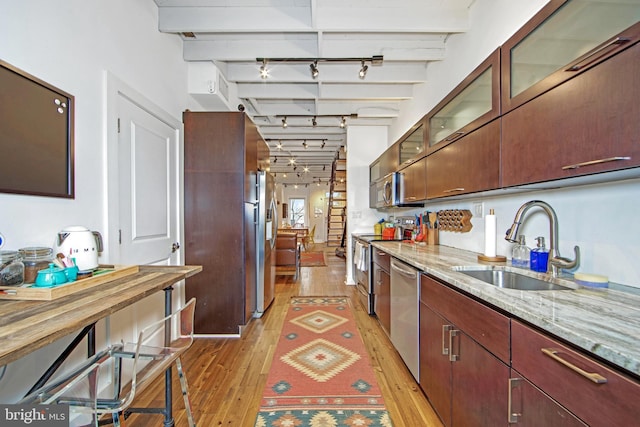 kitchen with track lighting, light wood-style flooring, beamed ceiling, appliances with stainless steel finishes, and a sink