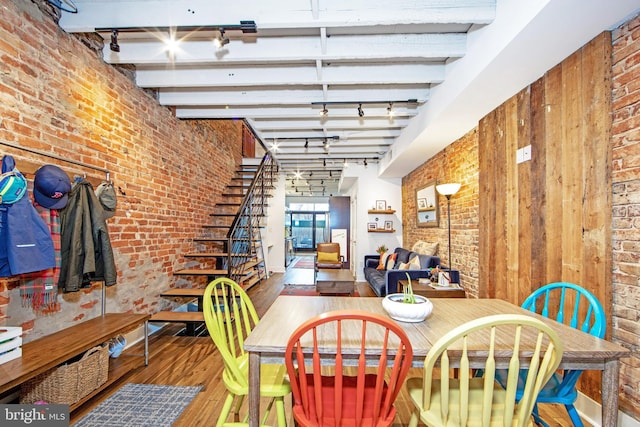dining room with wood-type flooring, track lighting, and brick wall
