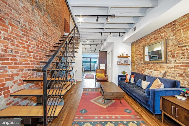 living room featuring rail lighting, brick wall, stairway, beam ceiling, and hardwood / wood-style flooring